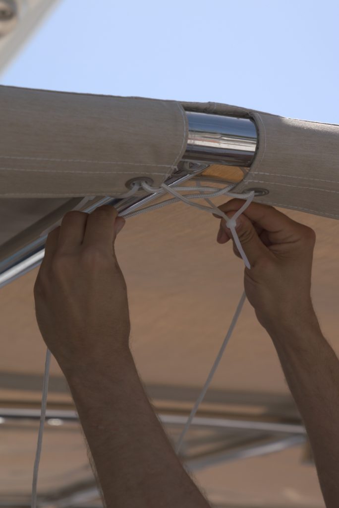Securing new, durable, aesthetically appealing beige sprayhood with strong white rope over frame, on Perini Navi Burrasca 56m.