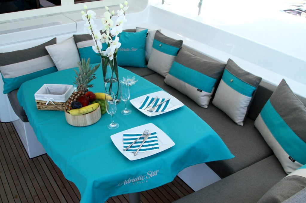 Dining area on Lagoon 52F deck saloon with personalised embroidered tablecloth & Frey Luxury Pillows Royal Ocean Collection.