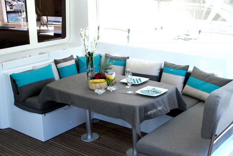 Dining zone on Lagoon 52F deck saloon with personalised embroidered tablecloth & Frey Luxury Pillows Royal Ocean Collection.