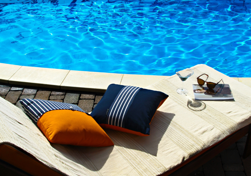 Total relaxation by the blue pool water with comfy deck chair cushions & luxury pillows in orange & dark blue stripes by Frey.