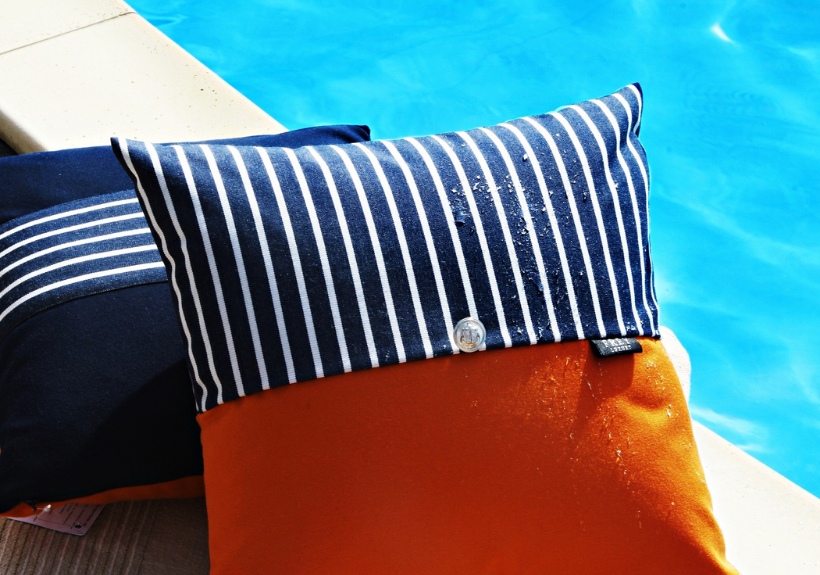 Frey Luxury Pillows in Sunbrella orange with dark blue & white stripes & silver button are water-repellent by your poolside.